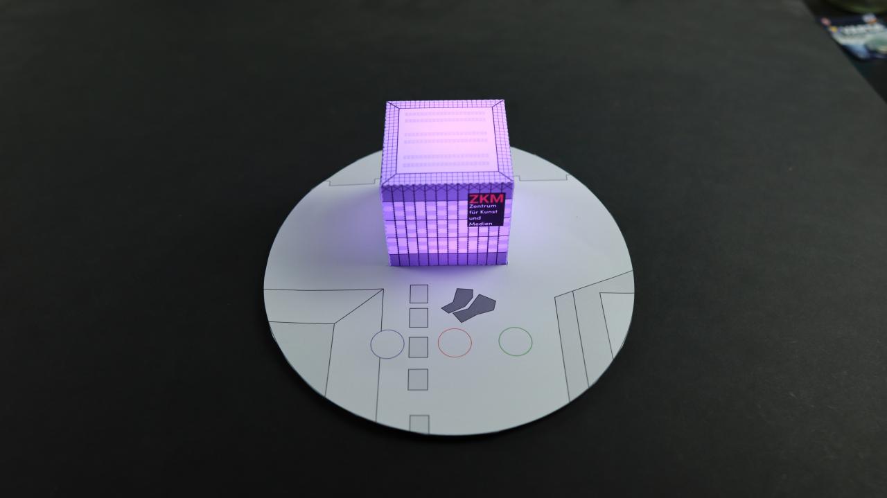 Eine Miniatur des ZKM Kubus zum Selberbasteln, der lila leuchtet.