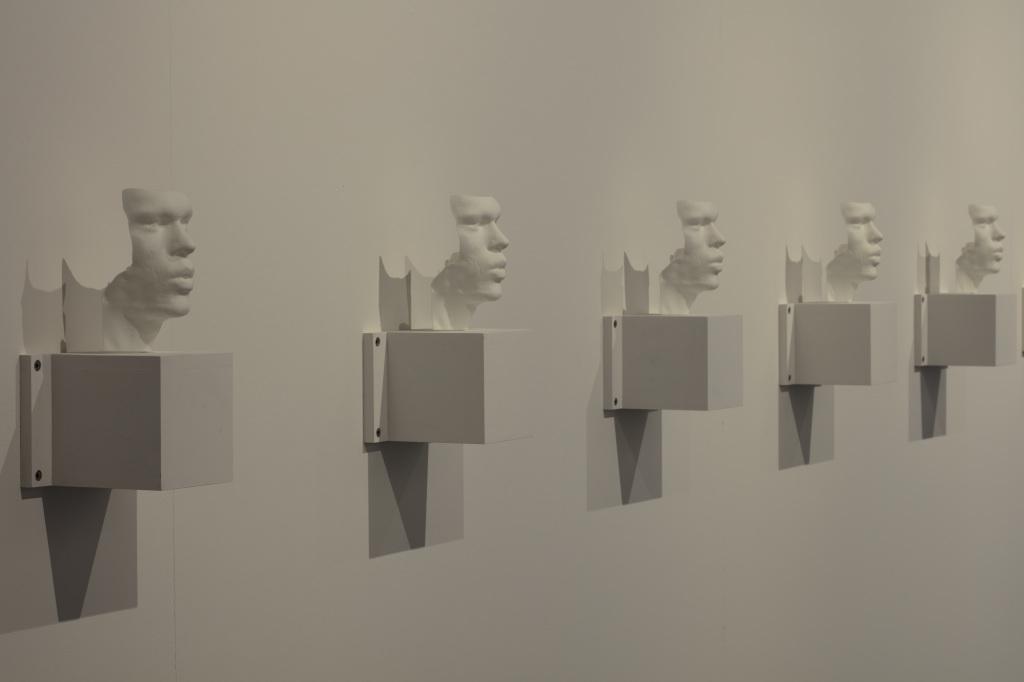  Several busts - 3D prints of the artists' vocal bands - hang side by side on a wall.