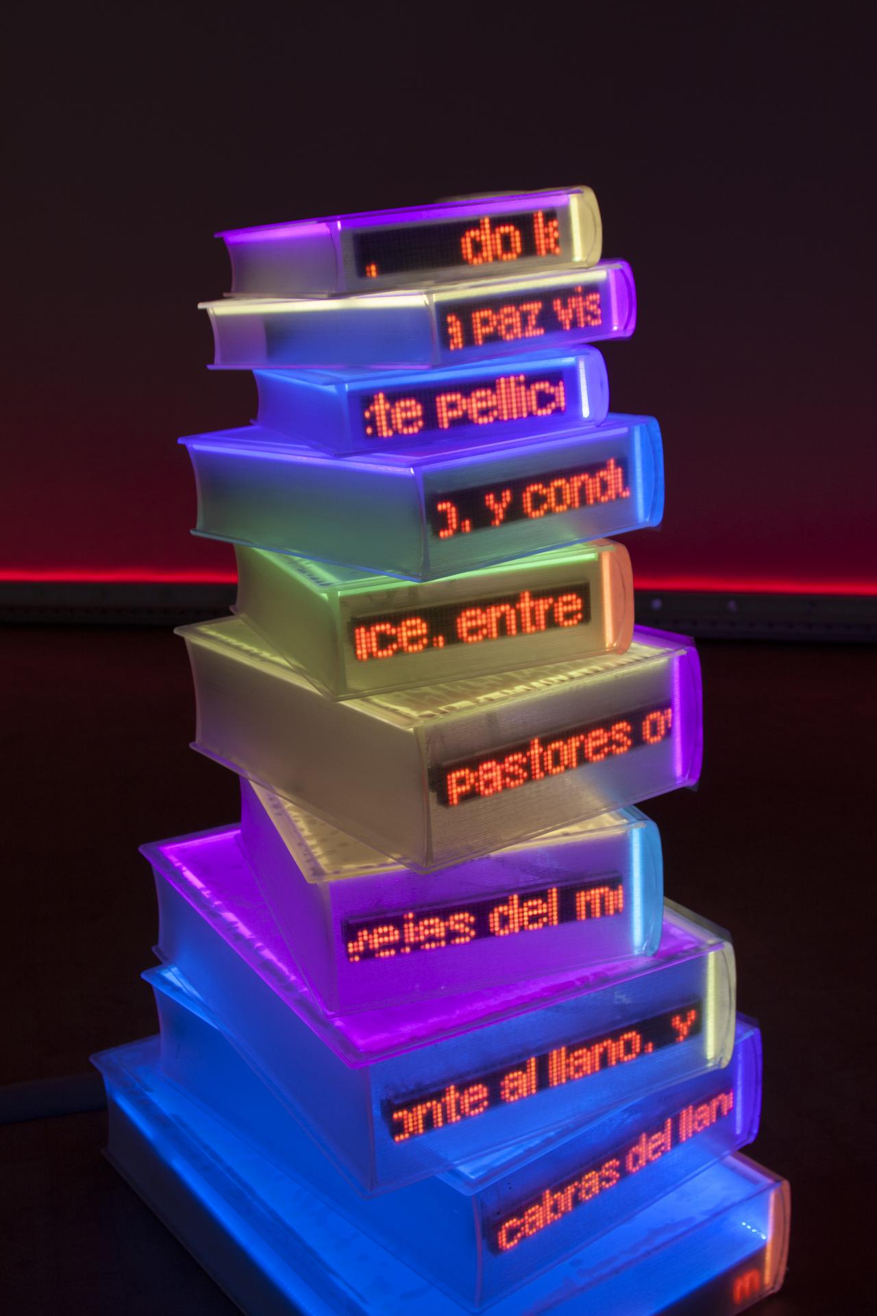 Colorfully illuminated books are stacked to form a sculpture.
