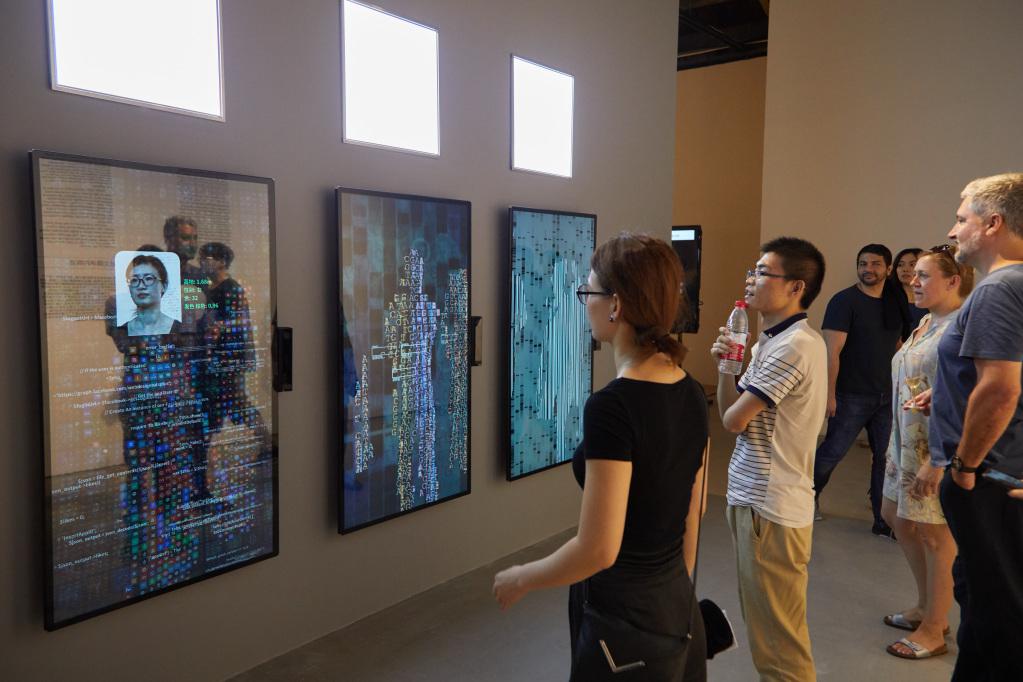 A woman stands in front of the artwork YOU:R:CODE that consists of large screens