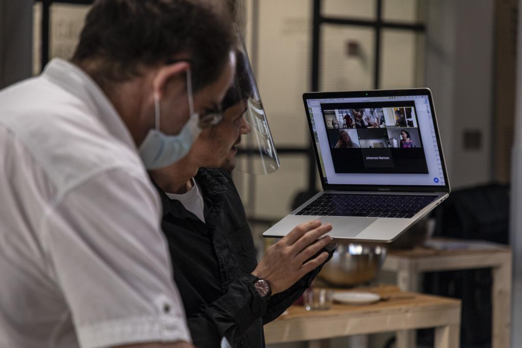 Ein Mann hält seinen Laptop hoch und zeigt anderen Teilnehmer:innen in einer Videokonferenz, was der Mann neben ihm vor sich hat.