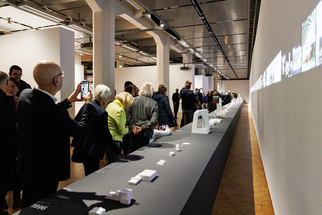 Besuchende der Ausstellung ole scheeren schauen sich die vielen kleinen 3D Drucke von geplanten Gebäuden des Architekten ole scheeren an