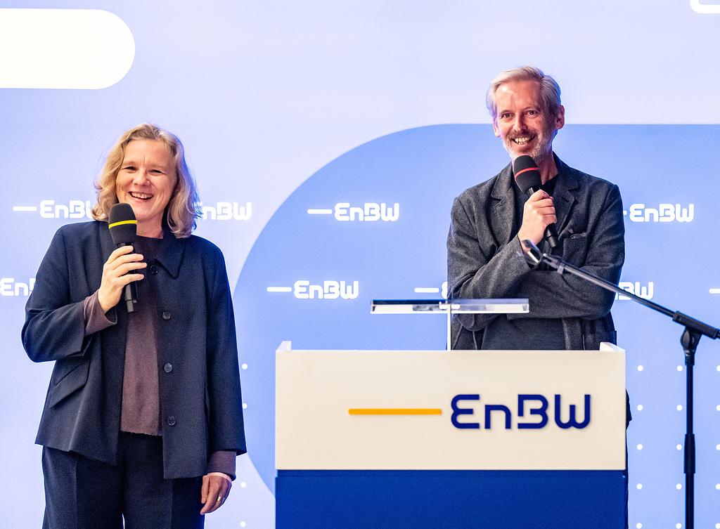 Helga Huskamp und Alistair Hudson, die beiden Vorstände des ZKM, stehen hinter einem Podest mit der Aufschrift EnBW und halten beide ein Mikrofon und lächeln.