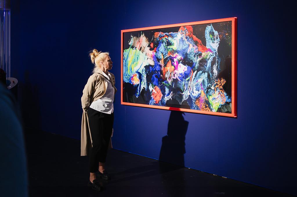 A woman stands in front of a colorful painting