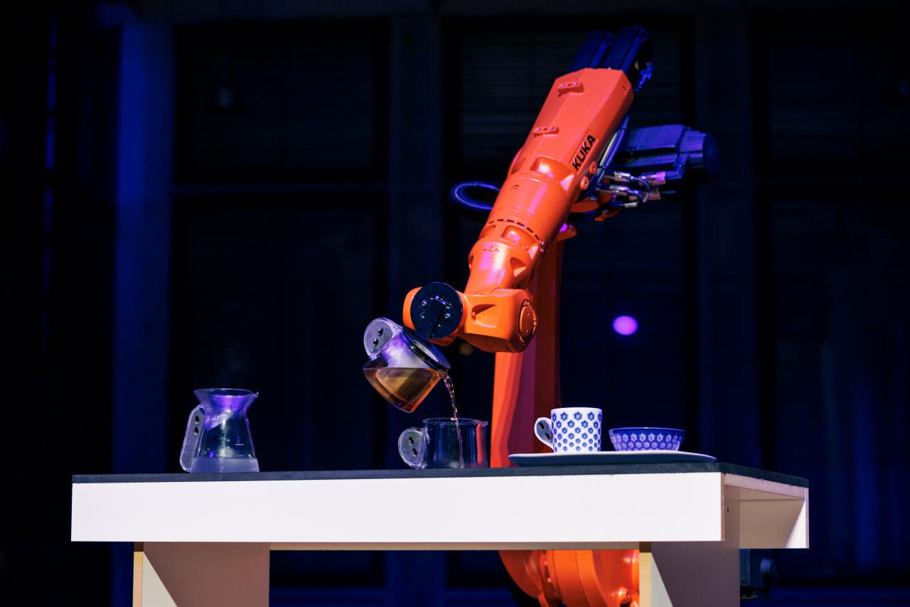 An orange robot pours tea into a small cup.