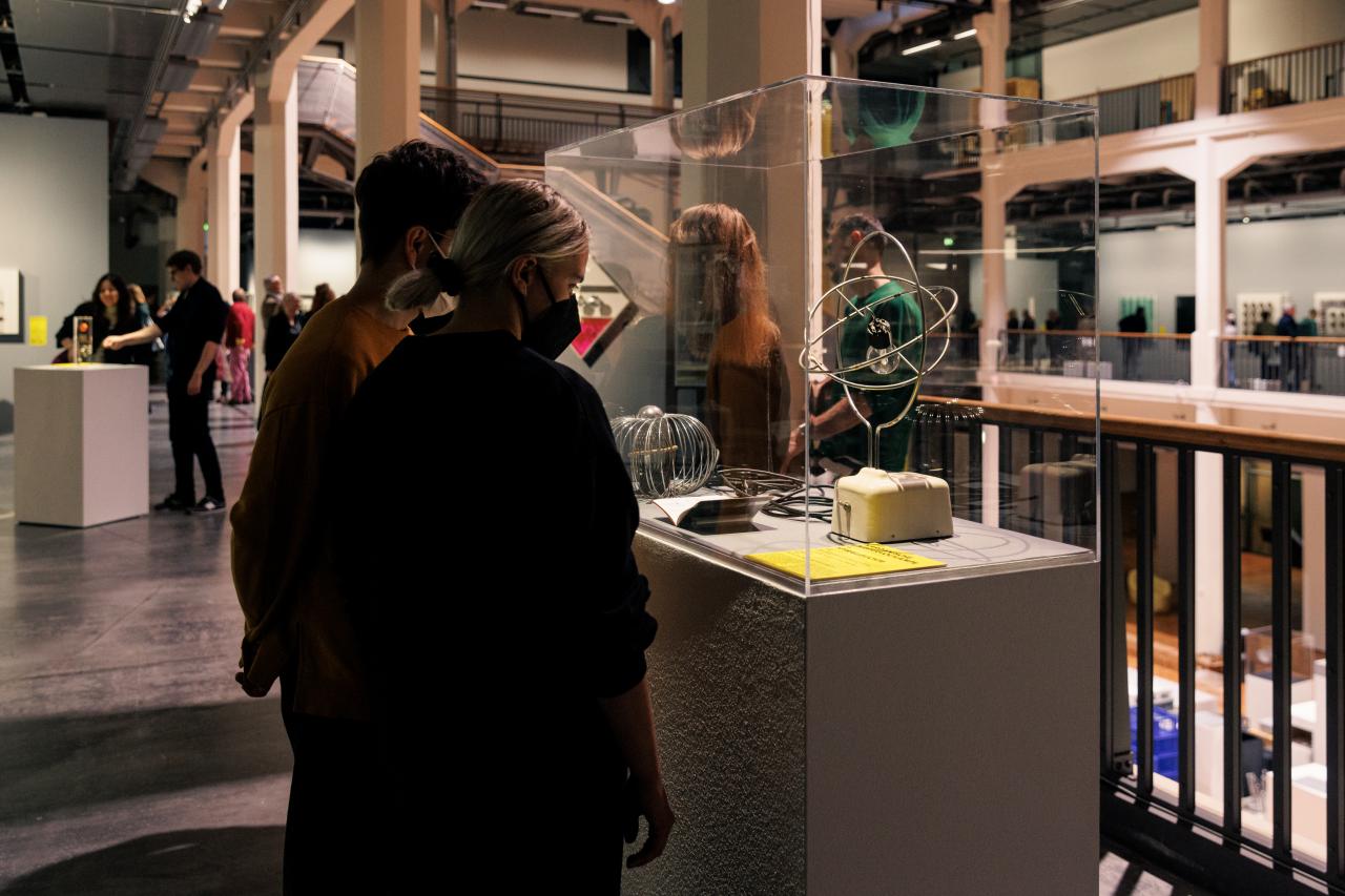You can see two people looking at a glass box. In this glass box is a wire frame, in which a light bulb is attached.