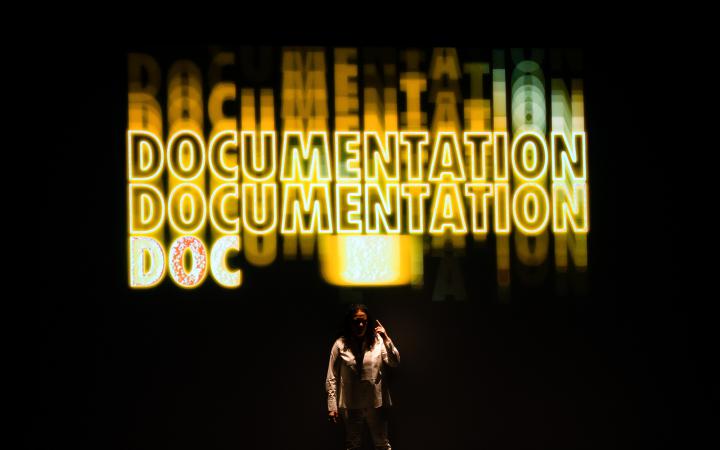 Noa Frenkel steht vor einem Hintergrund, auf dem mehrmals untereinander in groß »Documentation« geschrieben steht.