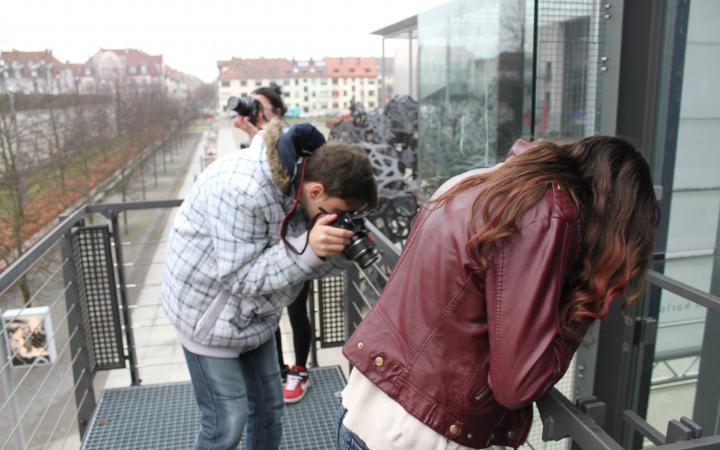 Three youngsters are taking photos on the stairs in front of the ZKM in different directions.