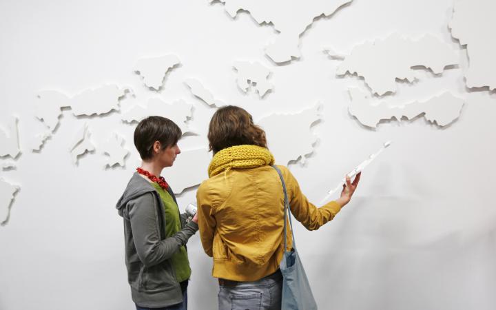 Two people in front of a white structured wall.