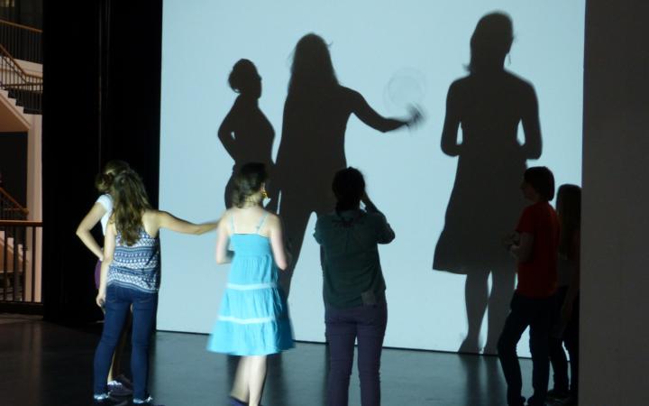 Children are standing in front of a wall where there shadows fall