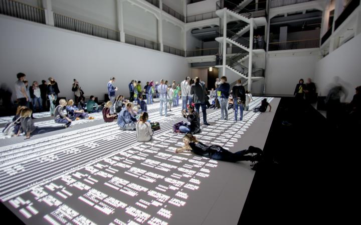 People sitting, lying and standing on a huge projection