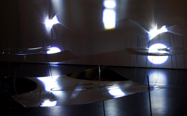  A dark room with delicate structures made of Plexiglas with shimmering liquids.
