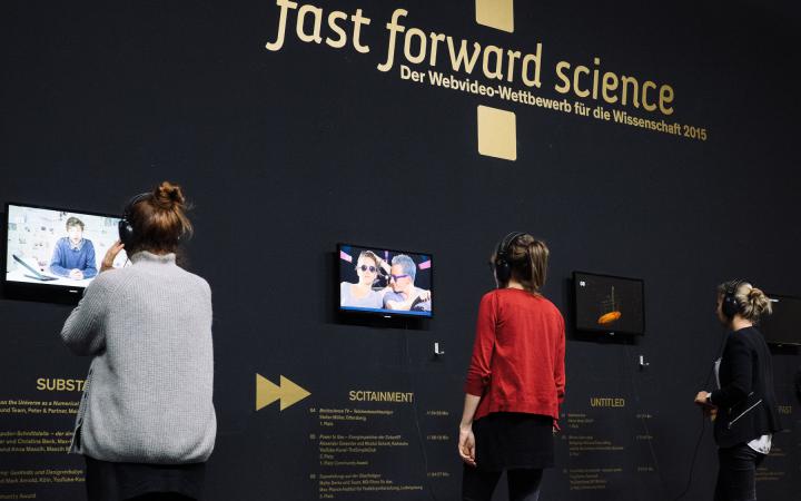 Three people with headphones on their ears look at different videos of the »fast forward science 2015« competition.
