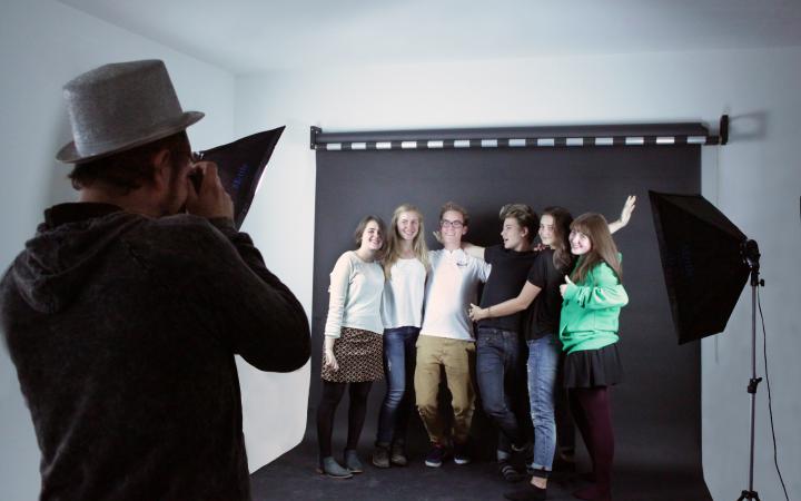 Eine Gruppe junger Menschen vor einer schwarzen Leinwand, die in die Kamera lächeln