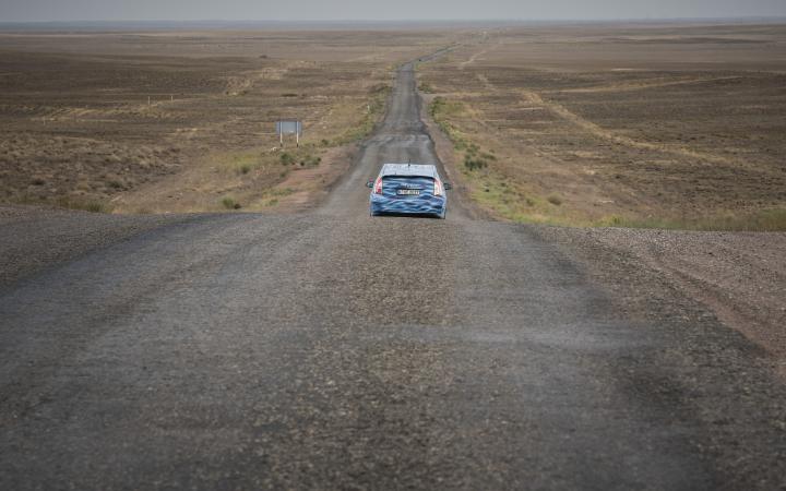 A blue car driving through a desert landscapes