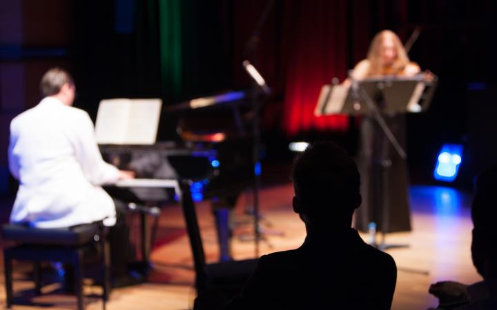Ein Mann in weißem Anzug am Klavier. Eine Frau im schwarzen Kleid spielt Geige.