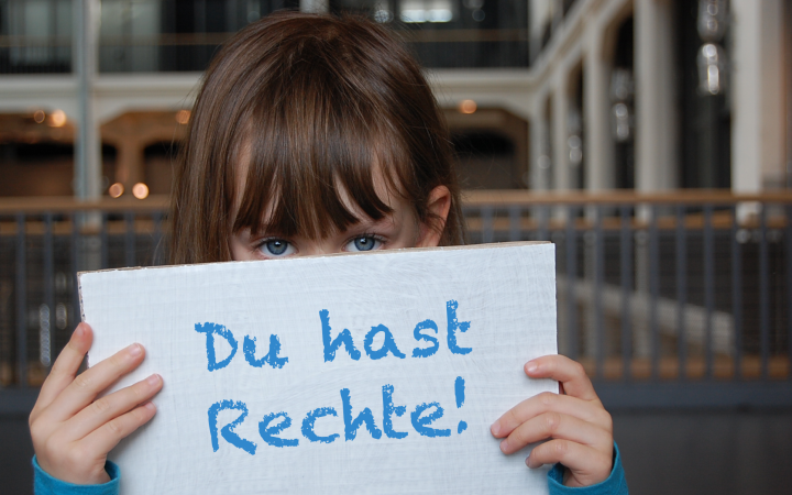 A little girl holding a placard in front of her face: "Du hast Rechte!"