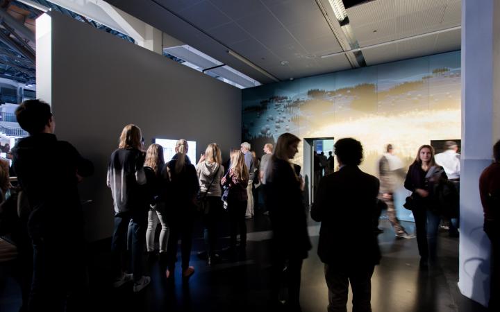 Many people standing in a room, looking at the artworks