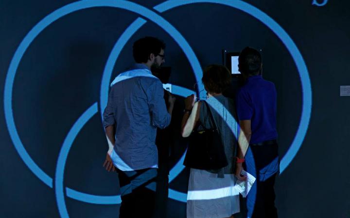 Three people standing in front of a wall. Blue circles are projected on them