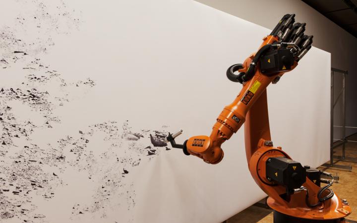 An industrial robot is drawing with pen on a large format.