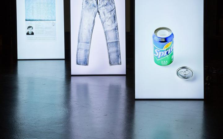 Three in a row standing luminous stands, on which a pair of pants, a sprite can and a card can be seen