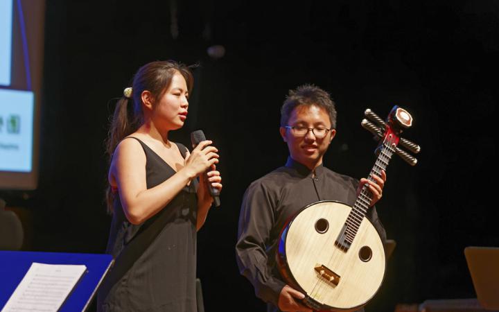 A woman with a microphone and a man with a kind of guitar