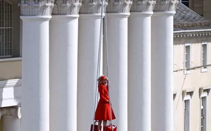 Eine blonde Frau in rotem Kleid auf einer schwebenden Treppe