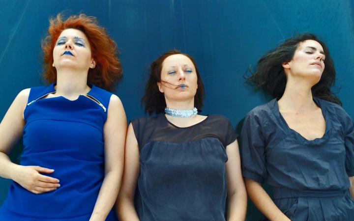 Drei Frauen, blau gekleidet und geschminkt, liegen auf der blauen Plane