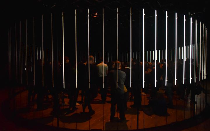 A circle of glowing neon tubes, many people standing in it