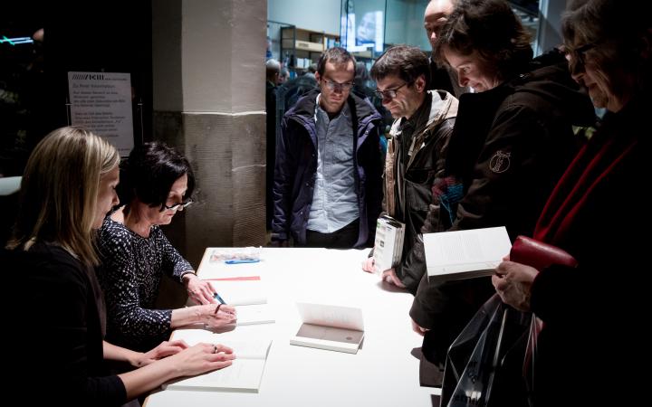 Menschen stehen vor einem Tisch, an dem eine Frau Bücher signiert