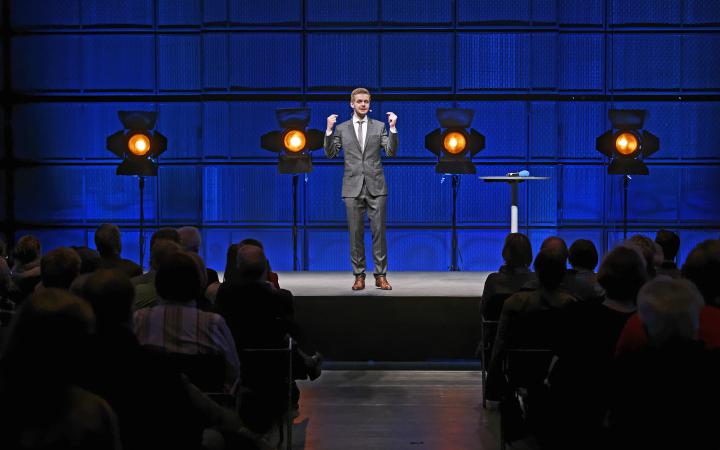 Ein Mann im Anzug steht auf einer Bühne.