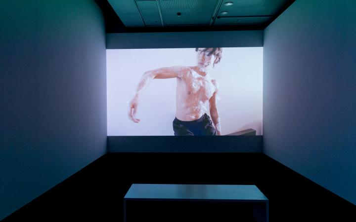 A shirtless dancer can be seen on a big screen