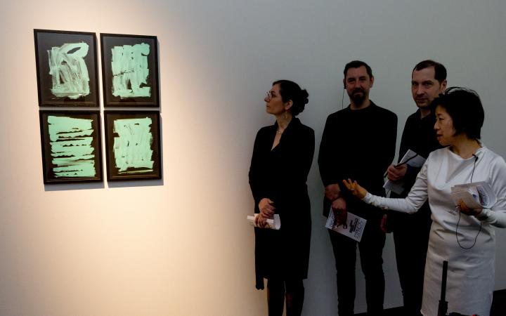 Four people looking at four images on which green brushstrokes are visible on a black background
