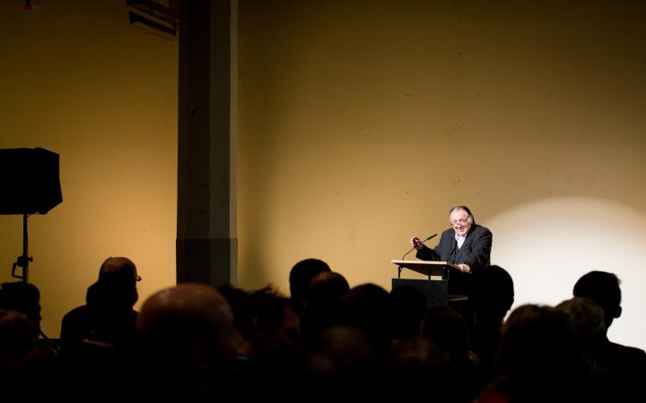 A man stands at a desk and talks to the audience