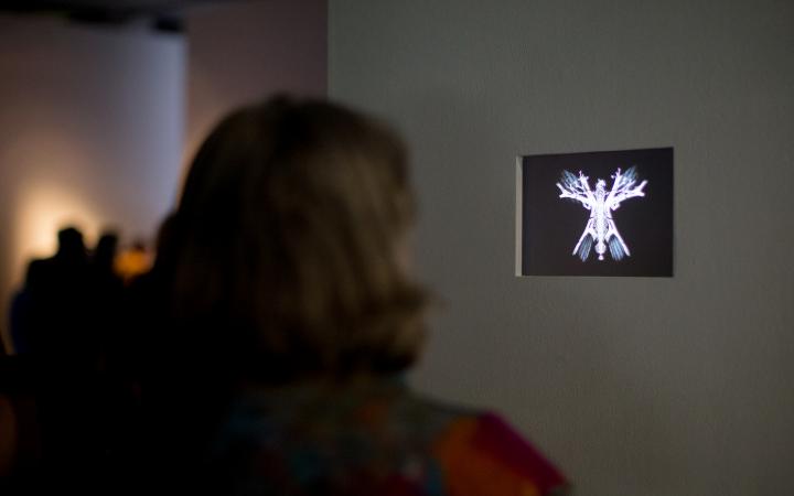 Eine Frau steht vor einem kleinen Bildschirm auf dem ein abstrakter, leuchtender Schmetterling zu sehen ist