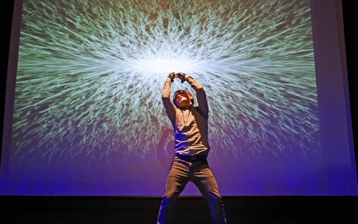 A man performs in front of a canvas on which a luminous ball can be seen