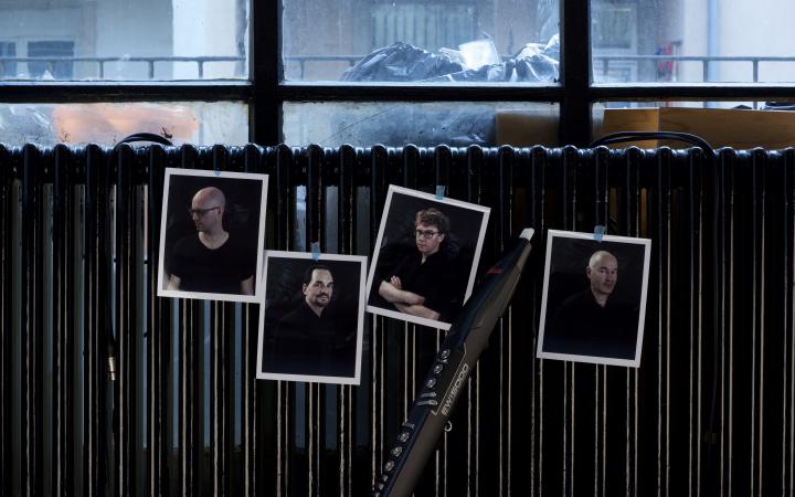 Vier Bilder von vier Männern kleben an einer Heizung. Dazwischen lehnt eine Klarinette.