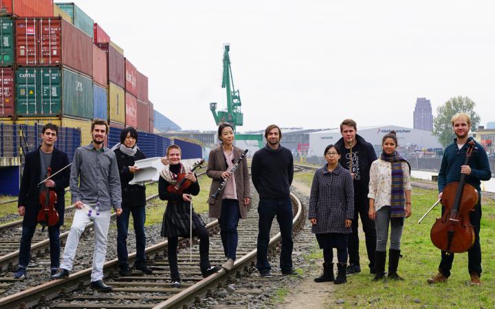 Das IEMA-Ensemble steht auf Schienen vor einer Hafenkulisse mit Containern und einem Kran