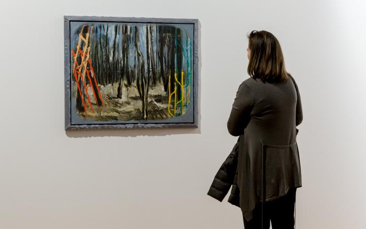 The picture shows a woman in front of a painting by Markus Lüperz