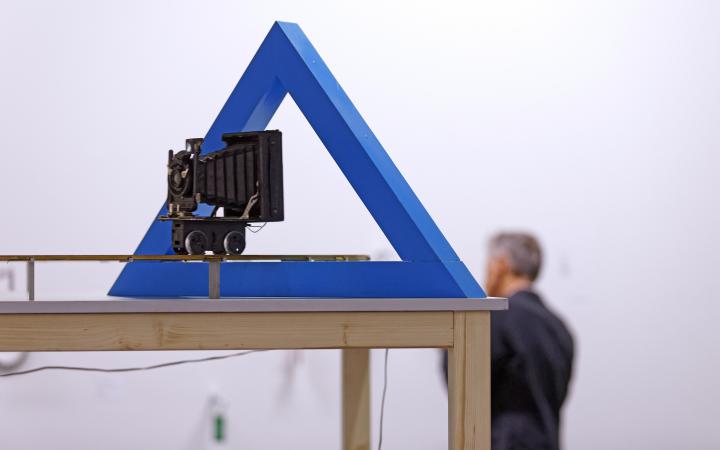 The picture shows a camera, which is directed by a hollow, blue triangle.