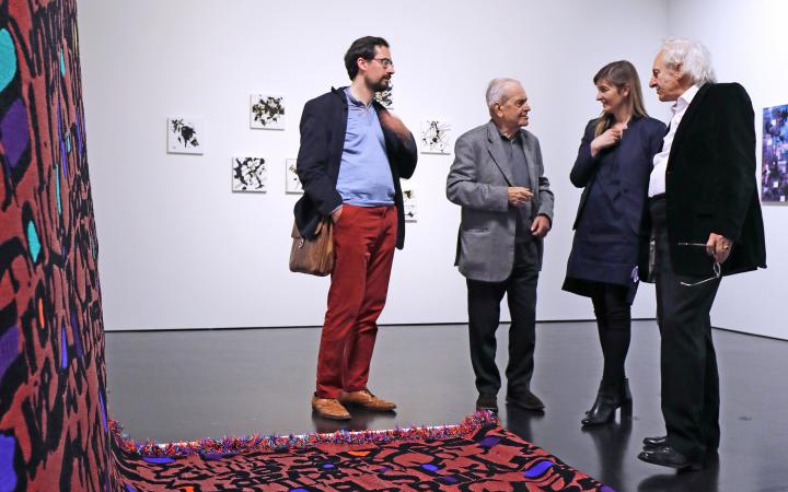 Vier Menschen stehen vor einem Werk, das aus einem langen roten Teppich mit Buchstaben besteht.