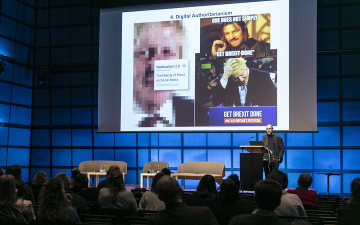 The photo shows Christian Fuchs during his lecture. The last lecture of the conference, in which he presents with current political pictures the debates about Trump and Boris Johnson