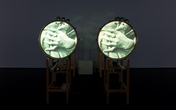 You can see two standing drums, each of which shows a picture of two hands folded into each other on the round surface. 