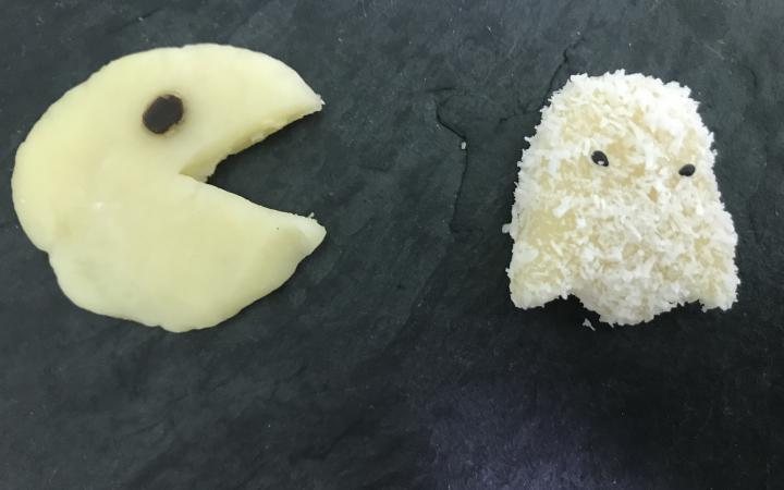 A pacman made of marzipan chases a ghost that is also made of marzipan and sprinkled with coconut flocks.