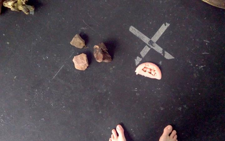 Two pieces of wood, three stones and a pair of feet can be seen on a black background. 
