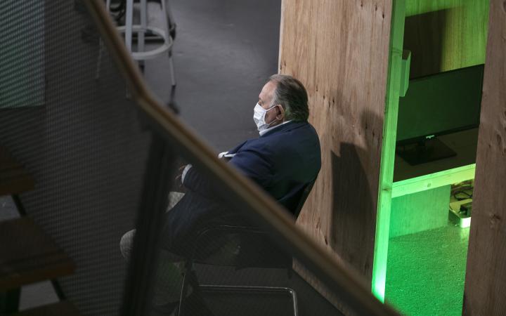 Peter Weibel sitzt mit einer Mund-Nasen-Schutz-Maske auf einem Stuhl und schaut aus dem Bild raus.