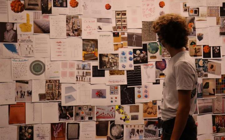 A teenager stands in front of a wall full of art sketches.