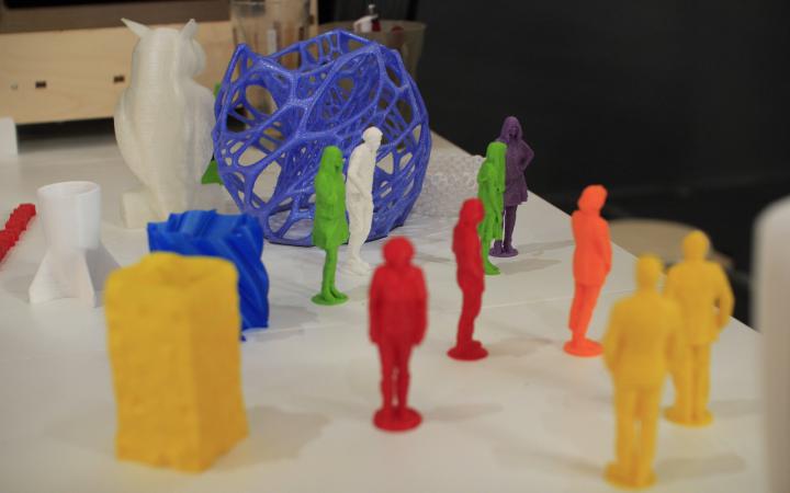 Kleine bunte Figuren, die dem 3D-Drucker ausgedruckt wurden, stehen kreuz und quer auf dem Tisch.