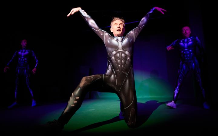 A man in futuristic armor strikes a pose in the spotlight on stage.