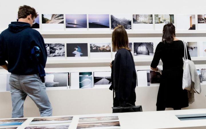 Drei Menschen betrachten Fotografien in einer Ausstellung
